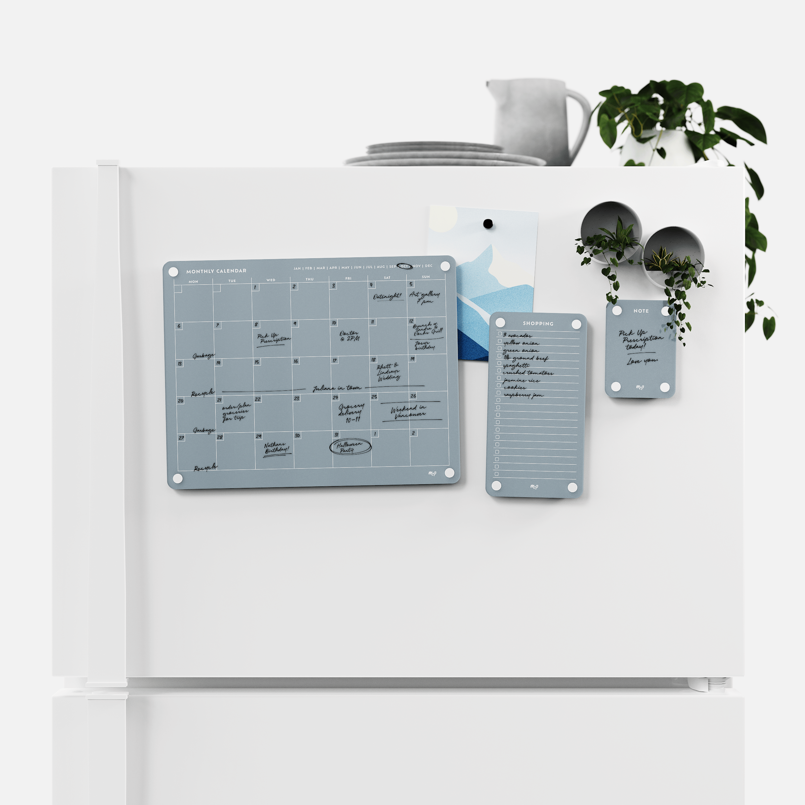 Slate grey monthly calendar, shopping list and note board magnetised to a white fridge door